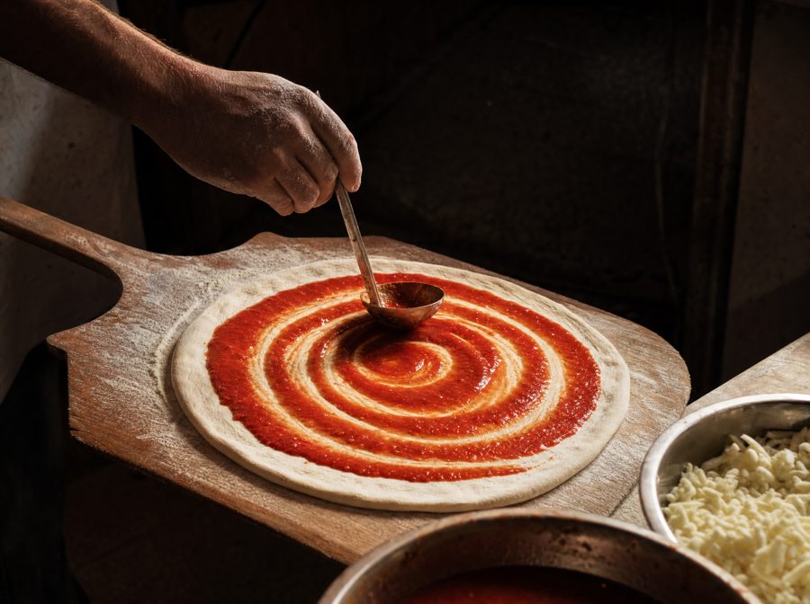 Ladling sauce onto stretched dough